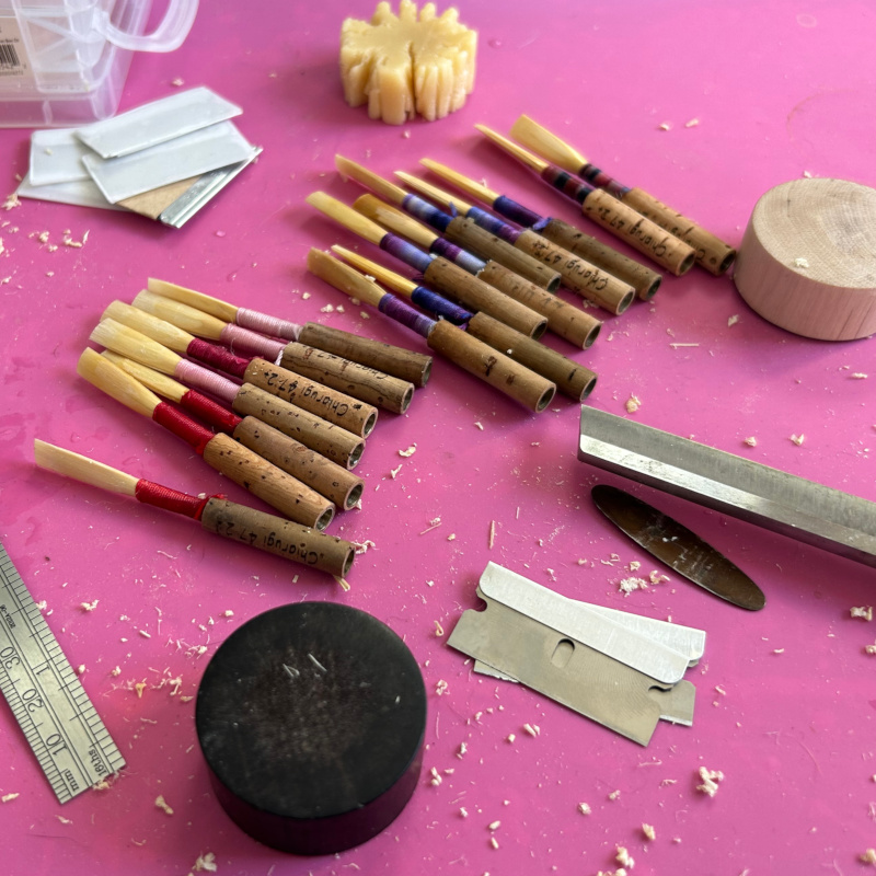 Several oboe reeds and reed making tools on a pink background