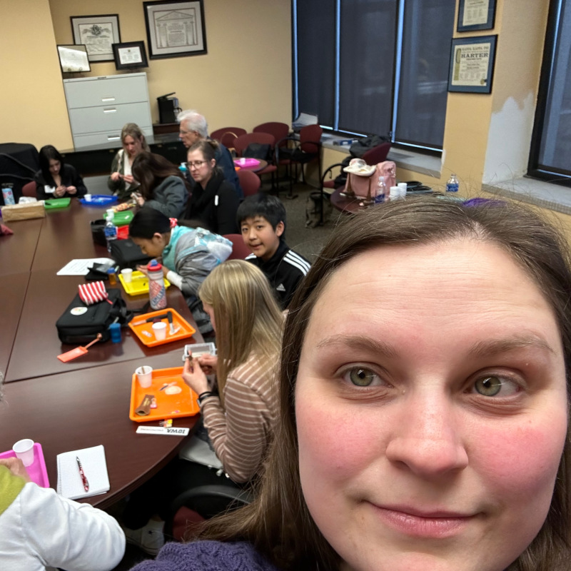 Several people sitting around large table working on oboe reeds, woman's face in foreground