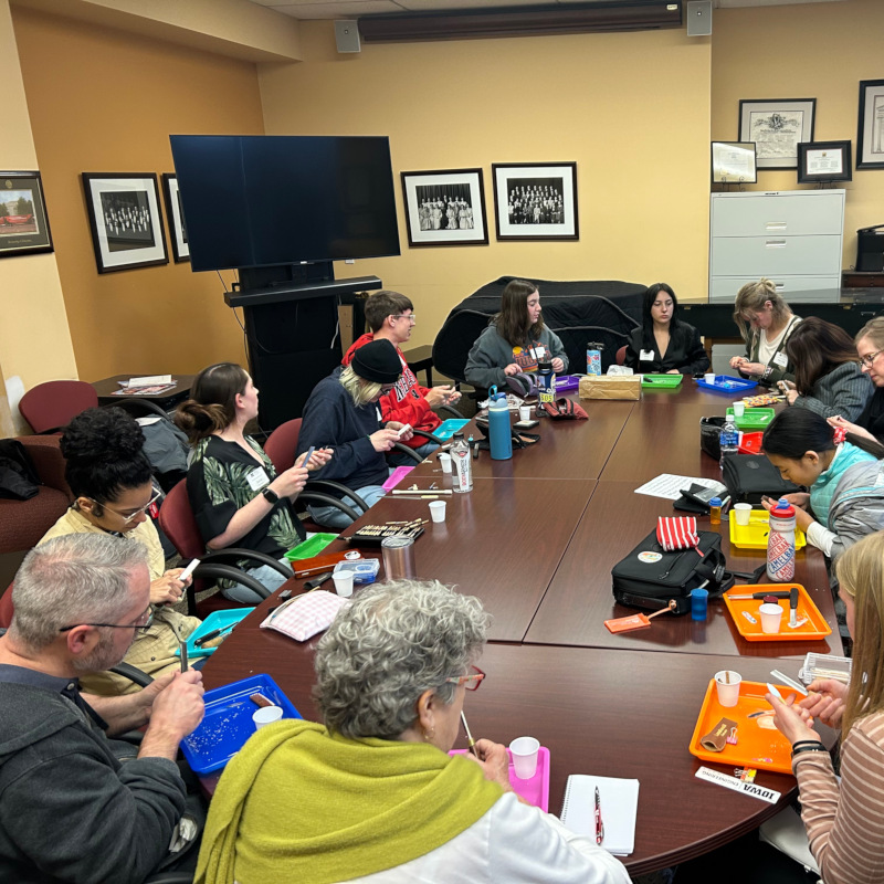 Several people sitting around a large table working on oboe reeds